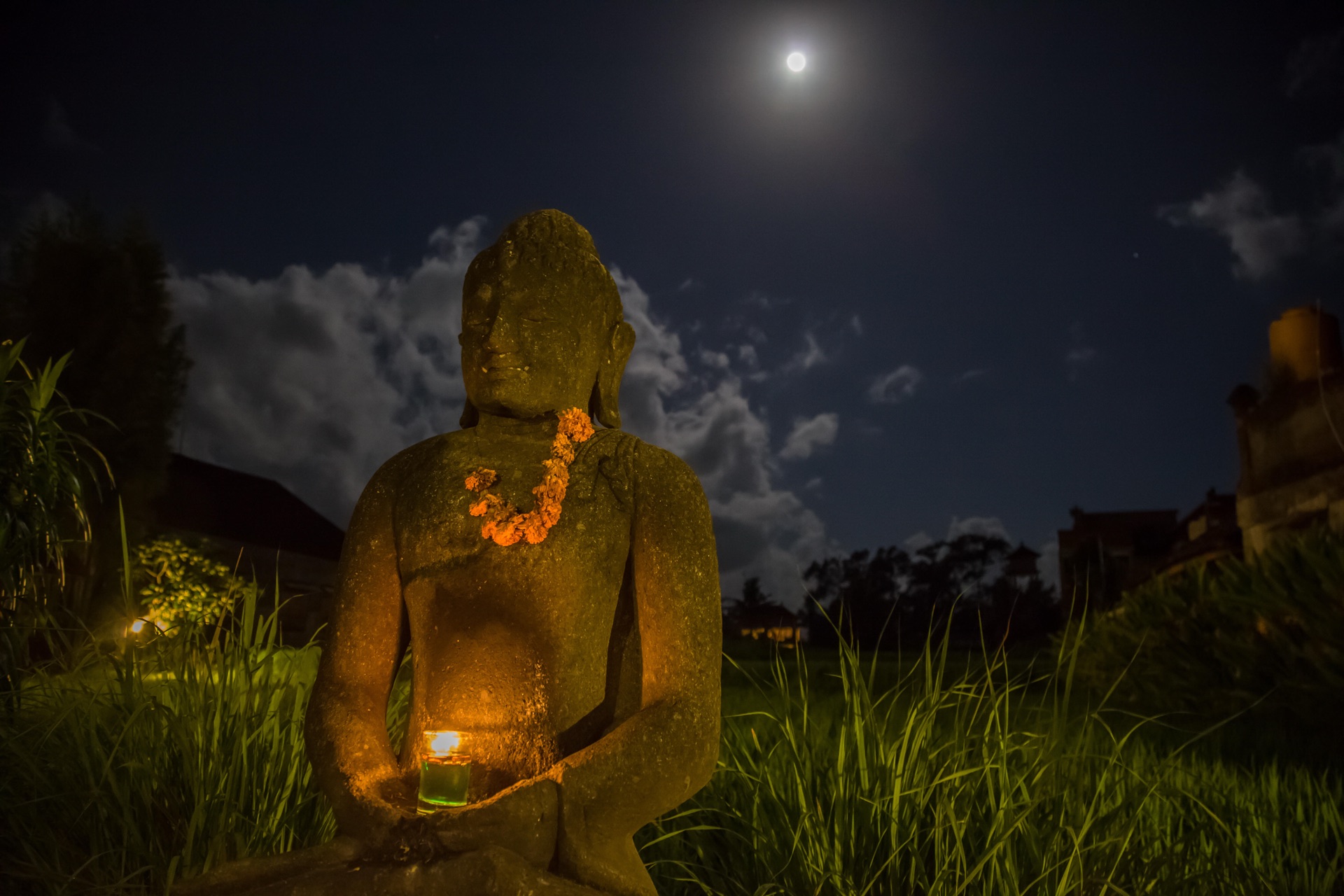 Statue de Bouddha sous la pleine lune, hibiscus orange en offrande